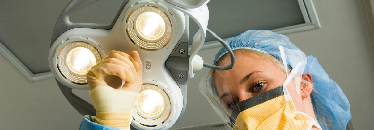 A woman in a surgical gown is operating a light fixture during a hysterectomy