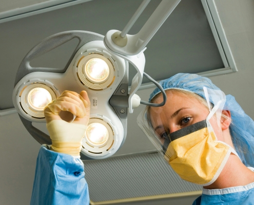A woman in a surgical gown is operating a light fixture during a hysterectomy