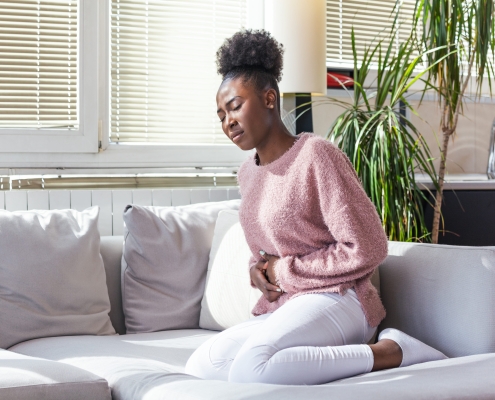 Woman with a stomach ache due to uterine fibroid embolisation sitting on sofa
