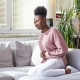 Woman with a stomach ache due to uterine fibroid embolisation sitting on sofa