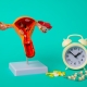 An anatomical model of a woman’s womb with a clock and medication comparing uterine fibroid embolisation vs. medication