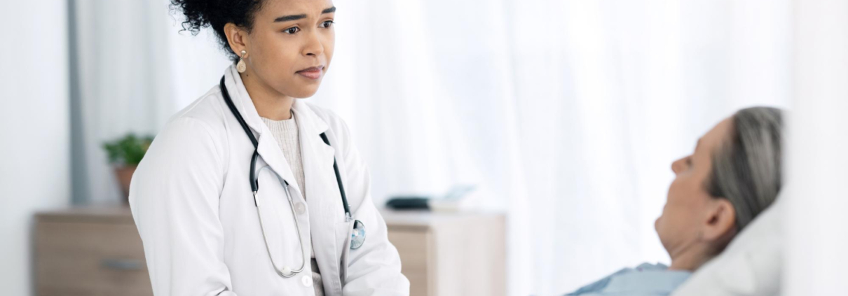 A young doctor explaining UFE vs radiofrequency ablation fibroids to a patient in a hospital bed.