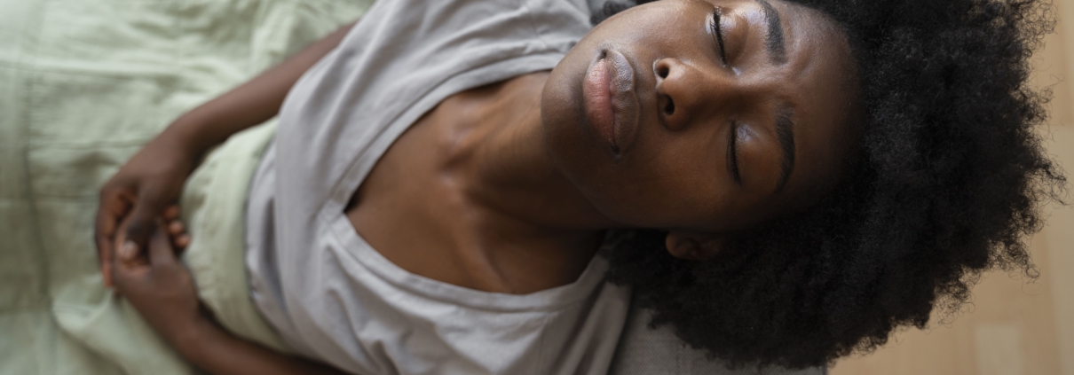 A young lady sitting on a couch and nursing uncomfortable symptoms of different types of uterine fibroids.