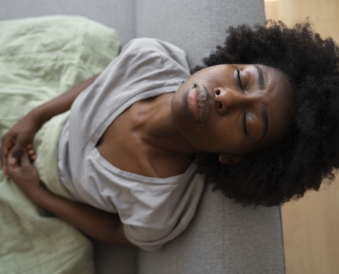 A young lady sitting on a couch and nursing uncomfortable symptoms of different types of uterine fibroids.