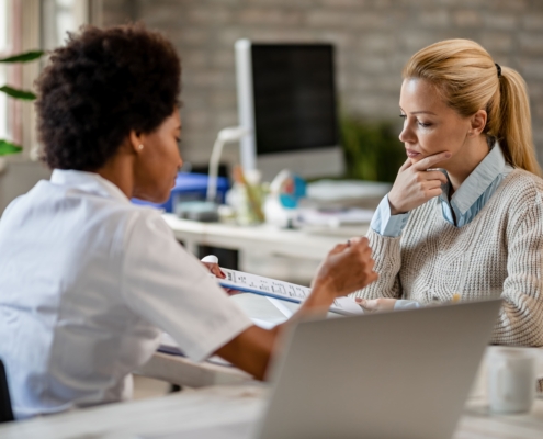 A young woman sitting with a nurse at a clinic and reviewing minimally invasive treatments for uterine fibroids