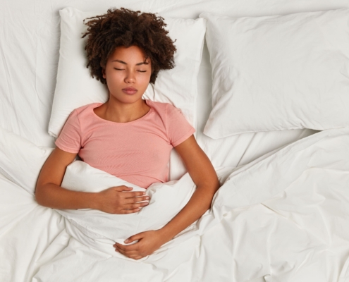 A young lady laying under the covers in bed, nursing her stomach while managing uterine fibroid embolization pain