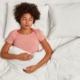 A young lady laying under the covers in bed, nursing her stomach while managing uterine fibroid embolization pain